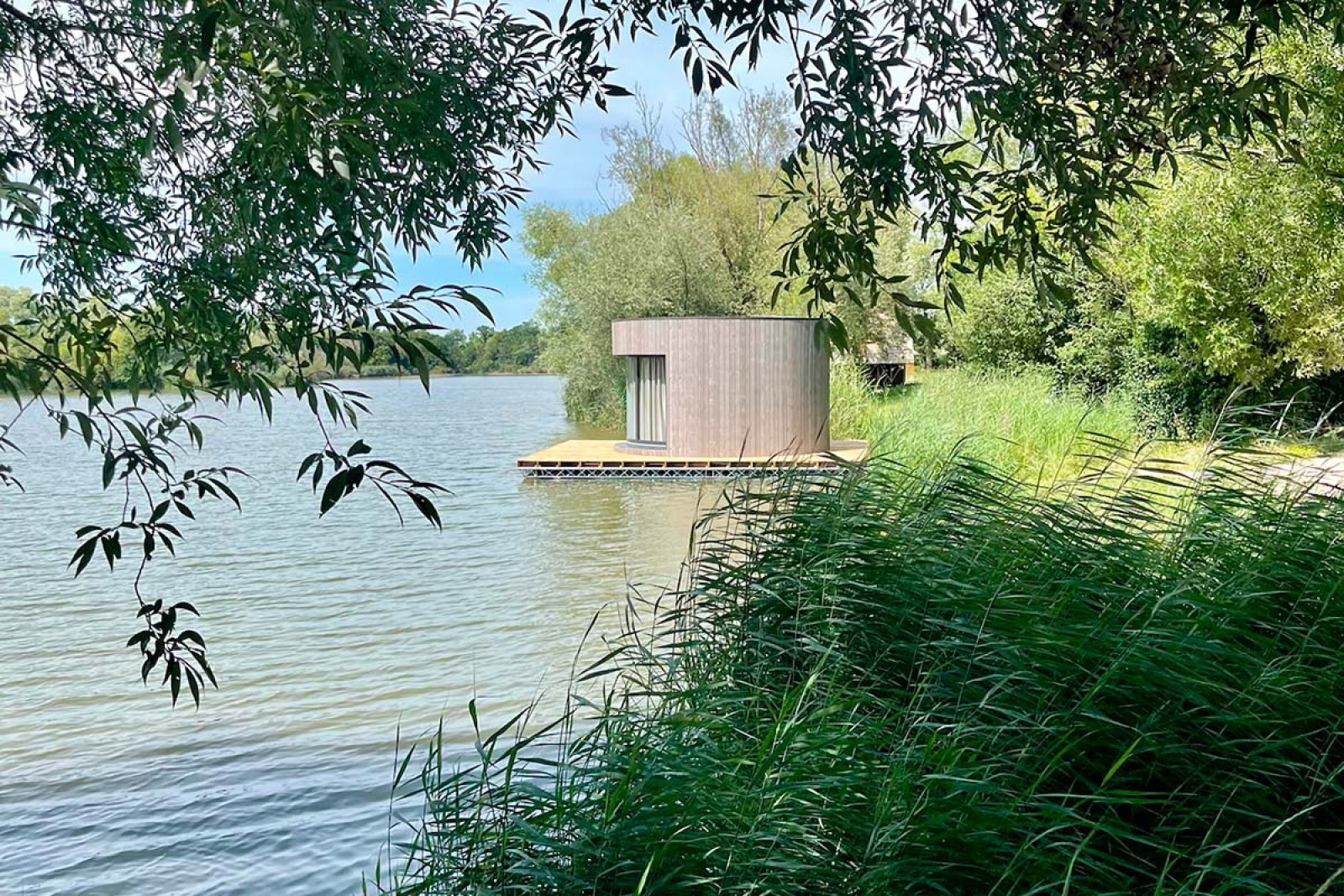 Ronde drijvende hut Lumipod Flottant bij Domaine des Feuilles in Frankrijk, omgeven door groen en water.