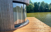 Finestra curva con tenda in una cabina sul lago su terrazza di legno presso Lumipod Flottant, Francia.
