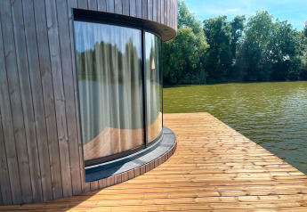 Finestra curva con tenda in una cabina sul lago su terrazza di legno presso Lumipod Flottant, Francia.