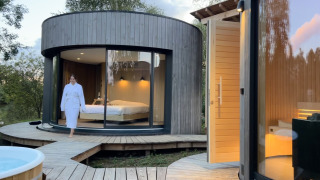 Donna in accappatoio esce da una moderna cabina rotonda in legno con grandi finestre al Lumipod Spa île.
