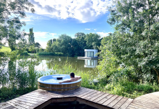 Persoon geniet van een buitenjacuzzi met prachtig zicht op een meer en een moderne hut in Frankrijk.