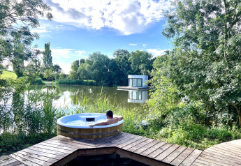Persoon geniet van een buitenjacuzzi met prachtig zicht op een meer en een moderne hut in Frankrijk.