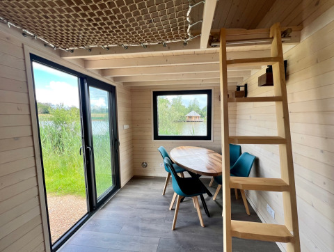 Innenraum eines Tiny House bei Domaine des Feuilles in Frankreich mit Tisch, Stühlen und Leiter.