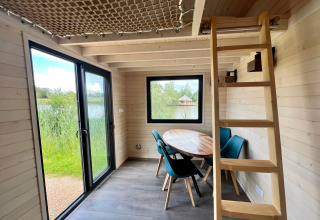 Innenraum eines Tiny House bei Domaine des Feuilles in Frankreich mit Tisch, Stühlen und Leiter.