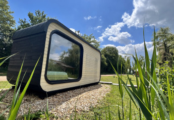 Roseaux Cabin-lodge van buitenaf gezien op een zonnige dag, met grote ramen en groen eromheen.