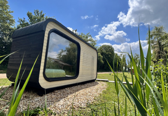 Roseaux Cabin-lodge van buitenaf gezien op een zonnige dag, met grote ramen en groen eromheen.