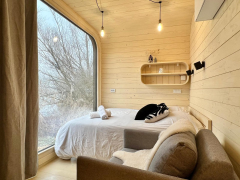 Knusse slaapkamer in de Roseaux Cabin bij Domaine des Feuilles, Frankrijk, met groot raam en natuurzicht.