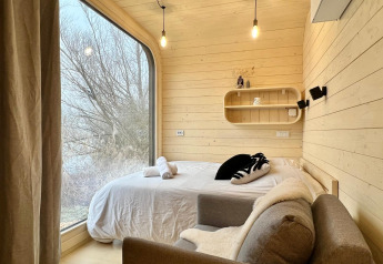 Knusse slaapkamer in de Roseaux Cabin bij Domaine des Feuilles, Frankrijk, met groot raam en natuurzicht.