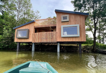 Moderna Spa Horizon Cabin su palafitte vicino all’acqua, vista da una barca, circondata da alberi.