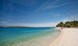 Plage idyllique du Camping Brioni en Istrie, Croatie, avec eau limpide, arbres et ciel dégagé.