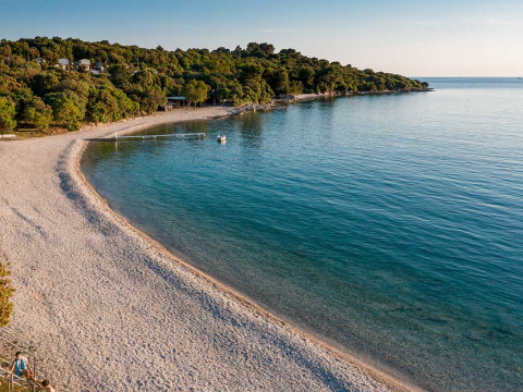 Rustige strand en helder water bij Camping Brioni vakantiepark in Istrië, Kroatië, omgeven door bos.