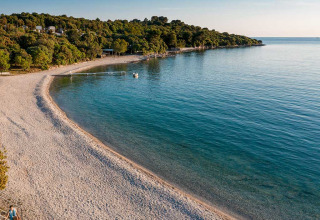 Peaceful pebbly beach and calm blue sea at Camping Brioni holiday park in Istria, Croatia, with forest views.
