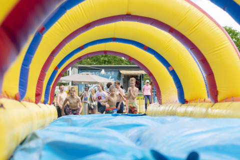Kinderen rennen enthousiast naar een opblaasbare waterglijbaan op Camping De Betteld in Gelderland.