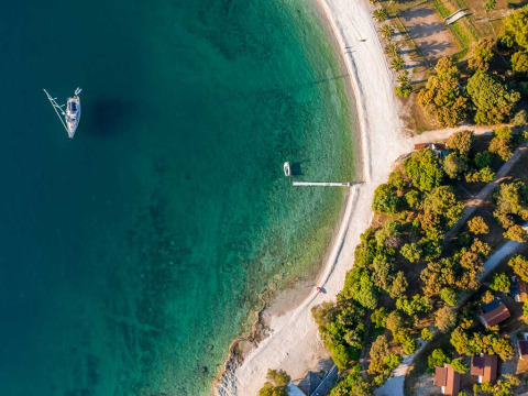 Luftfoto af Camping Brioni i Istrien, Kroatien, med klart blåt vand, båd og strand omgivet af træer.