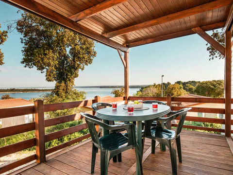 Vue du chalet Brioni Home Seaside au Camping Brioni, Croatie, avec table et chaises sur terrasse couverte.