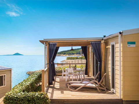 Zonnig terras met ligstoelen en eettafel bij Valamar Camping Marina met uitzicht op zee in Istrië, Kroatië.