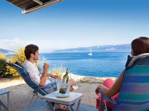 Two people relax with wine on camping chairs, enjoying a sea view at Valamar Camping Marina in Istria, Croatia.