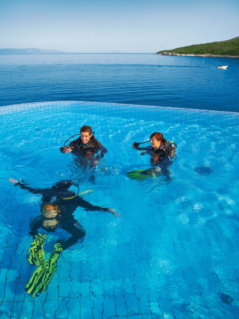Three divers practice scuba skills in a pool overlooking the sea at Valamar Camping Marina, Istria, Croatia.