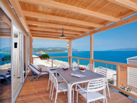 Overdekt houten terras met eettafel, ligstoelen en uitzicht op zee bij Valamar Camping Marina, Istrië, Kroatië.