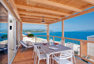 Overdekt houten terras met eettafel, ligstoelen en uitzicht op zee bij Valamar Camping Marina, Istrië, Kroatië.