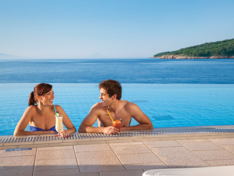 Pareja disfruta bebidas en la piscina infinita con vistas al mar en Valamar Camping Marina, Istria, Croacia.