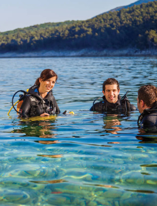 Tres personas con equipo de buceo disfrutan del agua cristalina en Valamar Camping Marina, Istria, Croacia.