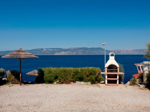 Seaside view at Valamar Camping Marina in Istria, Croatia, with a barbecue and thatched umbrellas in the foreground.