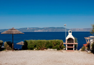 Seaside view at Valamar Camping Marina in Istria, Croatia, with a barbecue and thatched umbrellas in the foreground.