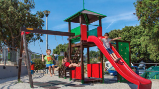 Niños juegan en un parque infantil con tobogán y columpios en Valamar Camping Marina, Istria, Croacia.