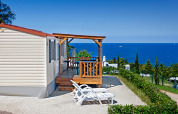 Lodge Orsera Home con veranda in legno, due lettini e splendida vista mare sotto il cielo azzurro.