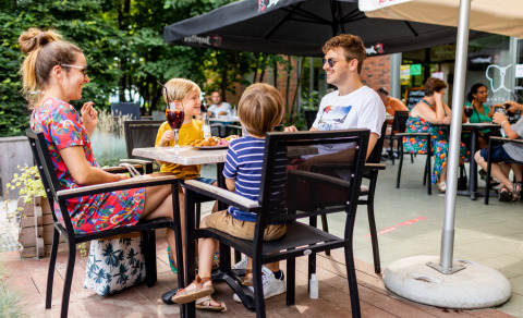 Gezin geniet van een zonnige lunch op het terras van Baalse Hei, een vakantiepark in Antwerpen, België.