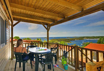 Woman relaxing on Orsera Home terrace at Camping Orsera, Croatia, overlooking scenic sea and boats.
