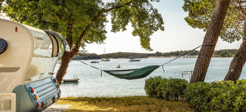 Sea view from a campsite at Camping Orsera in Istria, Croatia, featuring a hammock tied between trees and a caravan.