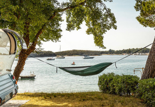 Vista al mar desde el camping Orsera en Istria, Croacia, con una hamaca entre árboles y una caravana cercana.