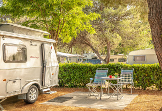 Area campeggio soleggiata a Camping Orsera, Istria, Croazia, con roulotte, tavolo, sedie e verde intorno.