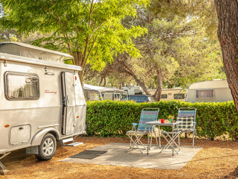 Schattiger Stellplatz im Camping Orsera in Istrien, Kroatien mit Wohnwagen, Sitzgruppe und Bäumen.