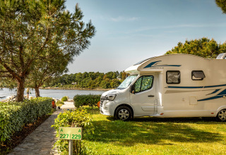 Camper parcheggiato su una piazzola verde vicino al lago al Camping Orsera, Istria, Croazia, tra gli alberi.