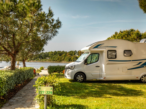 Wohnmobil steht auf einer grünen Parzelle am See im Camping Orsera, Istrien, Kroatien zwischen Bäumen.