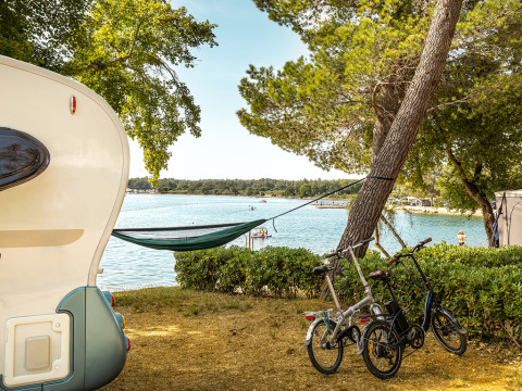 Vista dal Camping Orsera in Istria, Croazia, con roulotte, amaca e due biciclette vicino all’acqua.