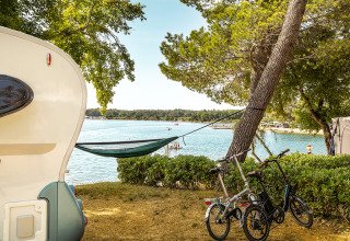 Blick vom Camping Orsera in Istrien, Kroatien, mit Wohnwagen, Hängematte und Fahrrädern am Wasser.