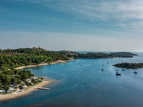 Vista del Camping Orsera en Istria, Croacia, con costa, árboles, barcos y un paisaje natural encantador.