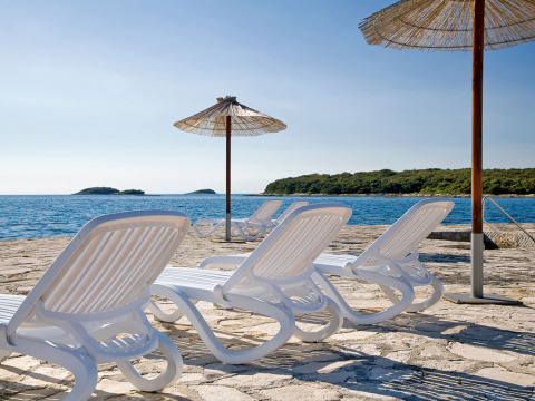 Lettini e ombrelloni al Camping Orsera in Istria, Croazia, con vista sul mare e su un’isola verde.