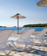 Ligstoelen en parasols bij Camping Orsera in Istrië, Kroatië, met uitzicht over zee en groen eiland.