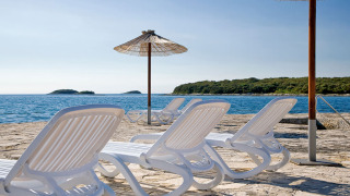 Ligstoelen en parasols bij Camping Orsera in Istrië, Kroatië, met uitzicht over zee en groen eiland.