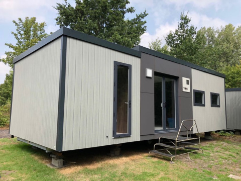 Moderne stacaravan op groene ondergrond bij Baalse Hei vakantiepark in Antwerpen, België, omgeven door bomen.