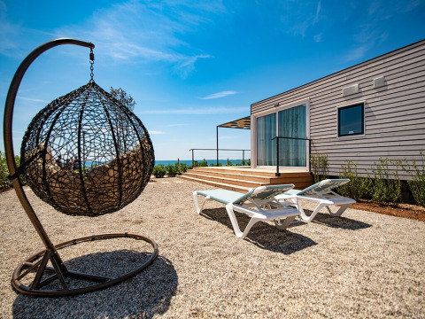 Außenbereich eines Camping Villa Chalets mit Hängesessel, Sonnenliegen und Blick aufs Meer.