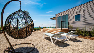 Outdoor area of Camping Villa chalet with hanging chair, sun loungers, wooden deck, and sea view.