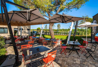 Espace repas extérieur avec chaises colorées et parasols au Camping Arena Grand Kažela, Istrie, Croatie.