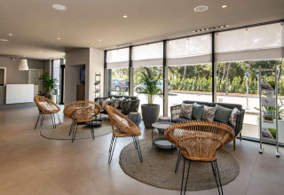 Helle Hotellobby mit modernen Rattanmöbeln, Sofas und großen Fenstern im Camping Arena Grand Kažela.