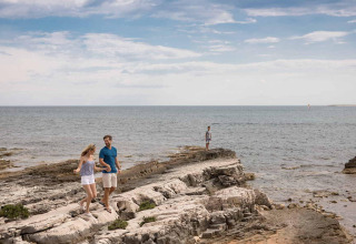 Una pareja camina sobre rocas en Camping Arena Grand Kažela, Istria, Croacia, con el mar al fondo.